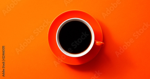 From above view of cup with black coffee placed on orange background