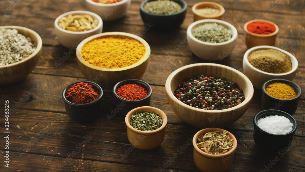 Arrangement of colorful spices and condiments in various bowls on shabby wooden table in daylight