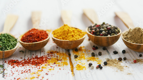 Row of wooden spoons filled with various multicolored spices and composed on wooden table © Dash