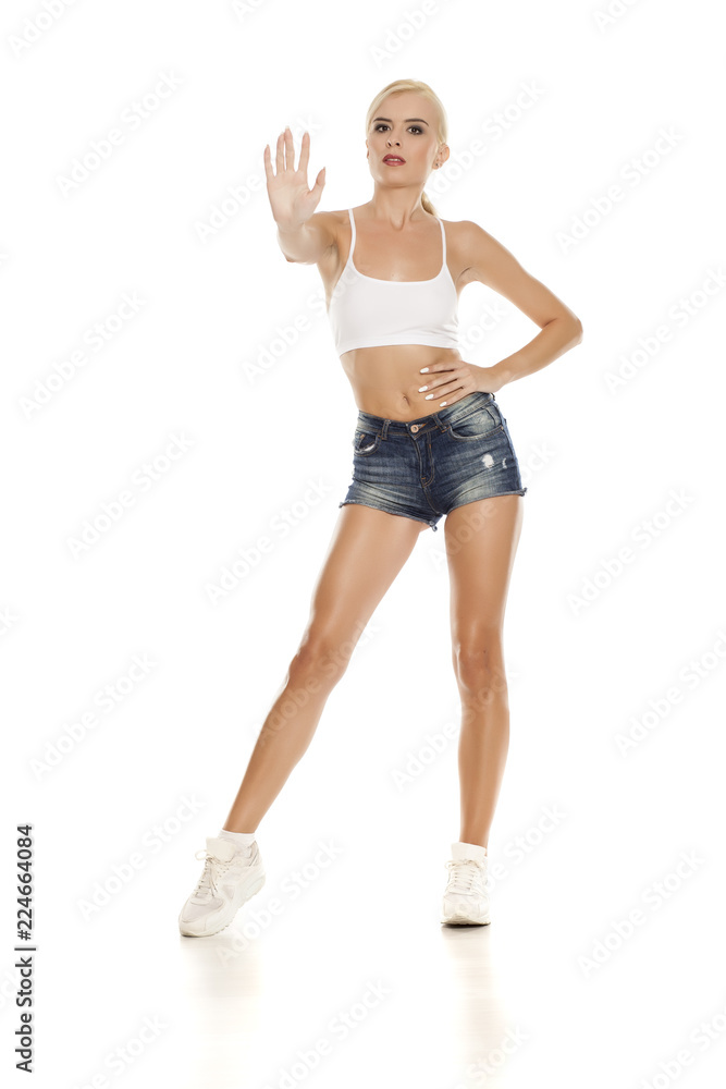 Young pretty woman posing in short jeans on white background, showing stop hand Young pretty woman posing in short jeans on white background, showing stop hand
