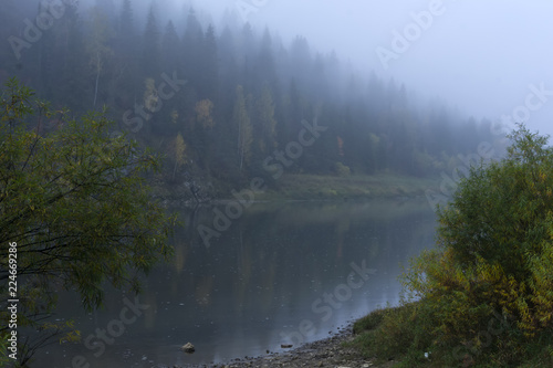 gloomy blurred autumn landscape with a misty river with rocky wooded shores..