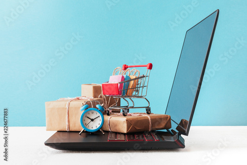 Internet shop / e-commerce sale and delivery service concept: shopping cart multicolored packages and boxes with trolleybus logo on laptop keyboard, blue background photo
