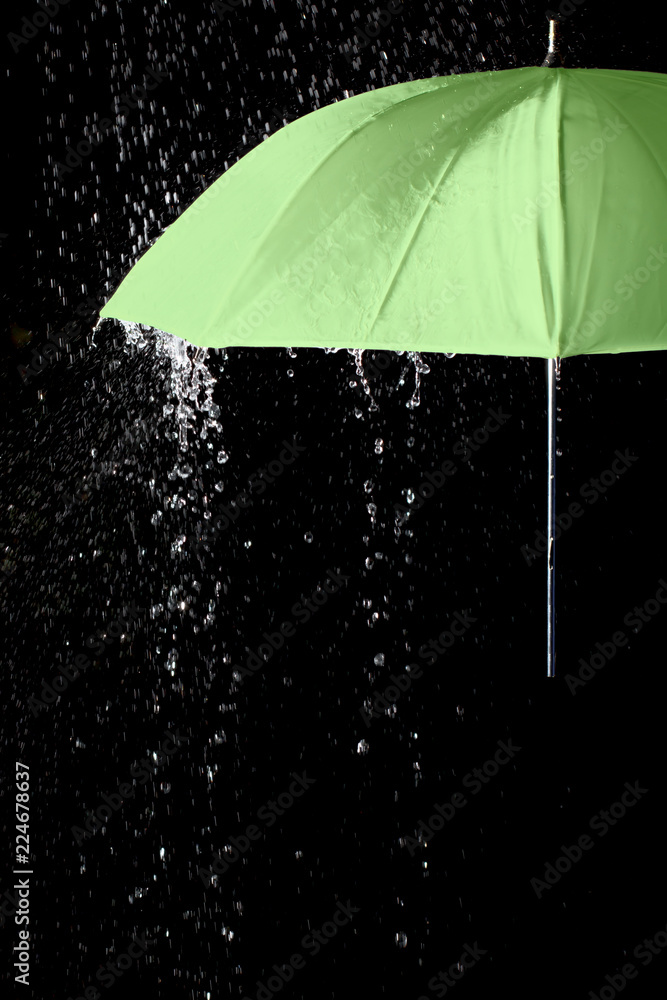Green umbrella under raindrops with black background