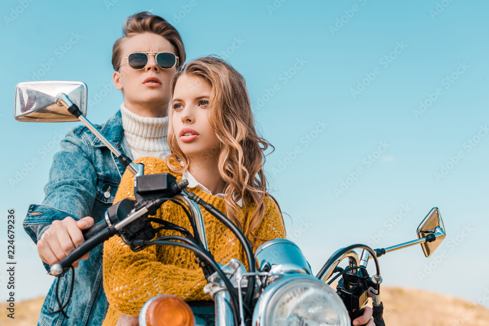 happy couple sitting on motorbike against blue sky