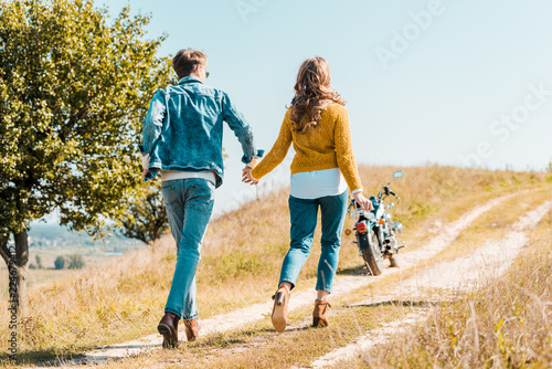 back view of couple walking on rural meadow and motorbike on background