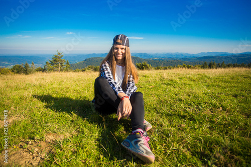 Woman tourist in cap on top of hill enjoying view of mountains. Travel concept