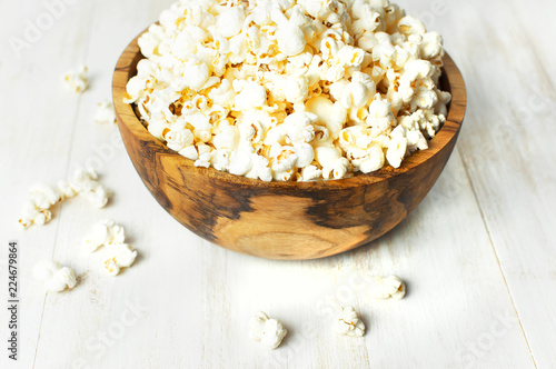 Brown wooden bowl with delicious traditional popcorn on a light wooden background. Top view of a light meal background.