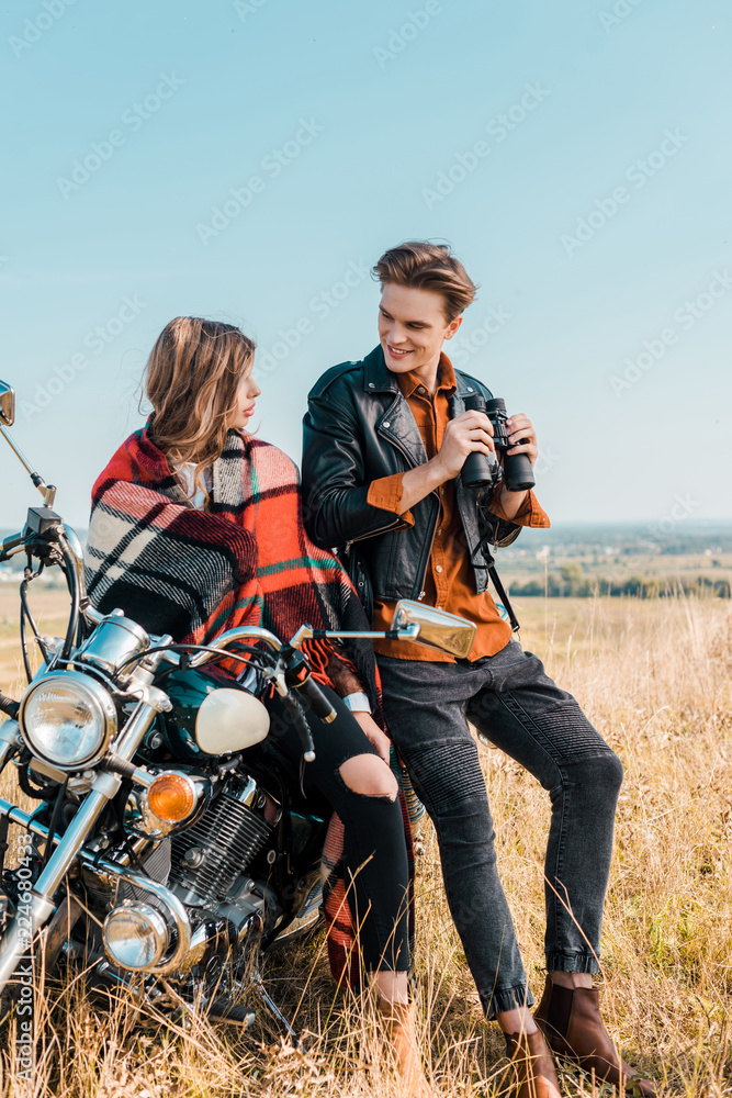 handsome boyfriend holding binoculars and looking at girlfriend sitting on motorbike