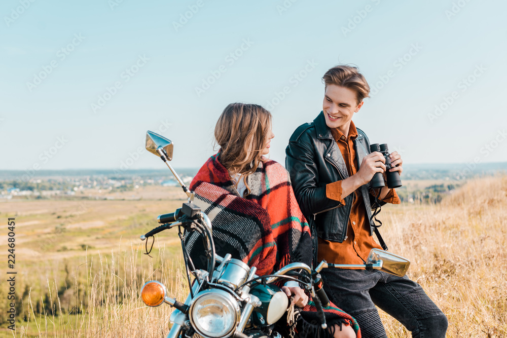 young boyfriend holding binoculars near girlfriend sitting on motorbike