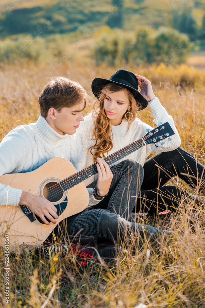 girlfriend looking at boyfriend playing guitar on meadow