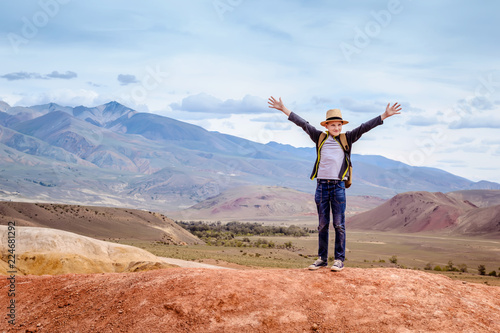 Happy boy traveler with his hands up on blue mountains background