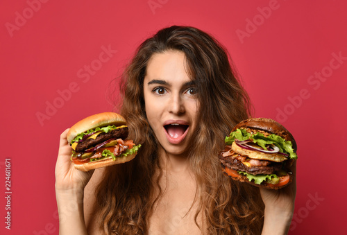 Woman hold two big beef burger sandwich and huge cheeseburger comparing with hungry mouth happy shouting on pink red 