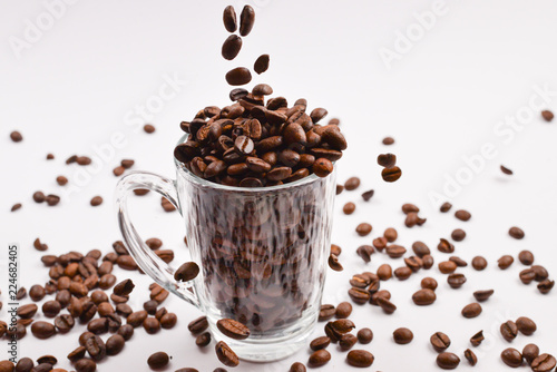 Grains of coffee are poured into a glass cup on a white background