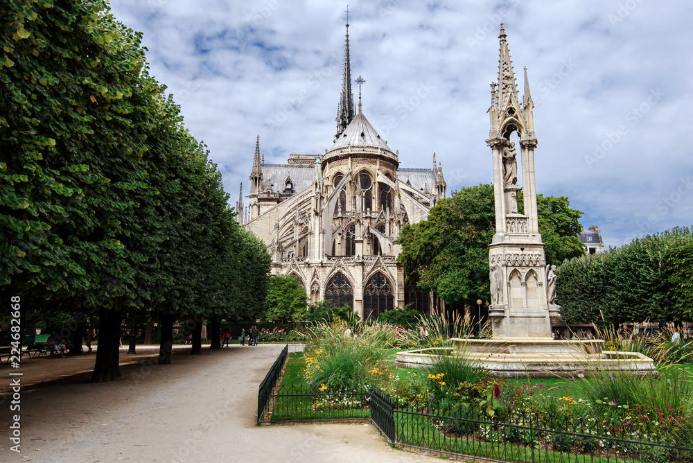 Paris, France - August 13, 2017. Medieval Notre Dame de Paris, most visited french monument of Gothic architecture. View from Square Jean XXIII - park with Virgin Fountain and flowers near Cathedral.