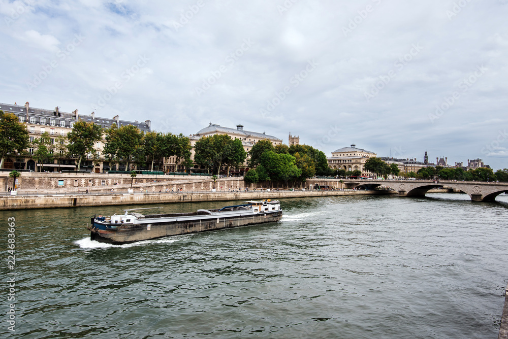 Obraz premium Paris, France - August 16, 2017. View of medieval Cite island and Pont au Change bridge from Seine riverside. Popular french landmark and tourist cruise boat in river Seine.