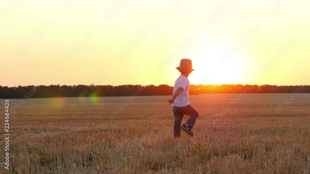 A child runs across the field in a straw hat during sunset. A child runs across the field in a straw hat during sunset.