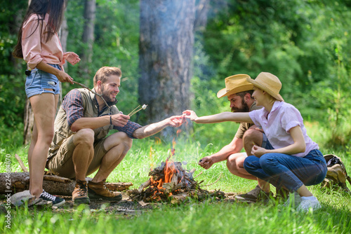 Camping activity. Company youth camping forest roasting marshmallows. Roasting marshmallows popular group activity around bonfire. Company friends prepare roasted marshmallows snack nature background