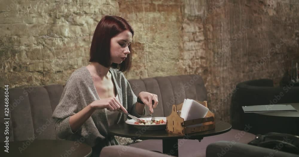 Attractive young woman eating vegetable salad. Interior cafe with old brick walls and low lighting. Attractive young woman eating vegetable salad. Interior cafe with old brick walls and low lighting.