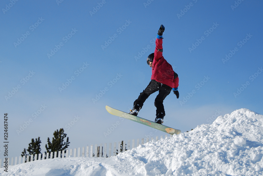 Male snowboarder on the snowy slope on sunny winter day. Young sportsman jumping, spraying snowflakes and flying on background of clear blue sky.