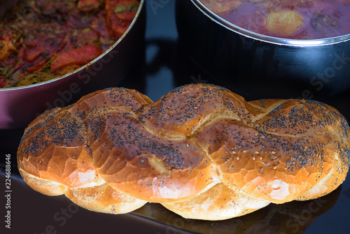 Hot plate for the Sabbath, a pot of spicy fish cooked with peppers and tomatoes,  pot of cholent or Hamin in hebrew and challah-special bread in Jewish cuisine. Traditional food for Jewish Shabbat. photo