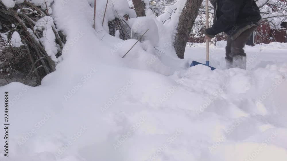 A man wearing warm clothes removing snow in a garden 