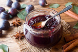 Plum jam in a glass jar. Fresh plum fruit on a wooden table.