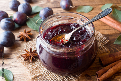 Plum jam in a glass jar. Fresh plum fruit on a wooden table.