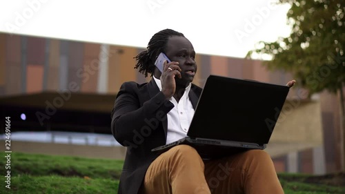 Corporate African man negotiating over the phone, while working outdoors on a laptop photo