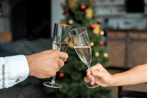 cropped image of couple celebrating christmas and clinking by champagne glasse at home