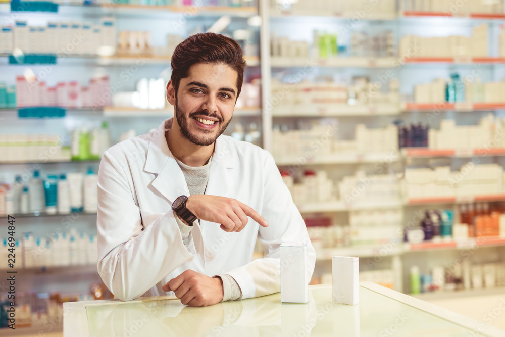 Friendly male pharmacist dispensing medicine holding a box of tablets Friendly male pharmacist dispensing medicine holding a box of tablets