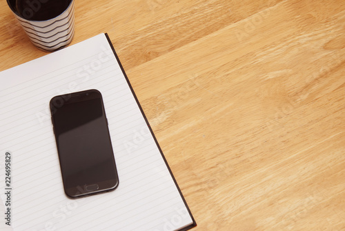 Open notebook with cup of coffee on wooden desk. Copy space.