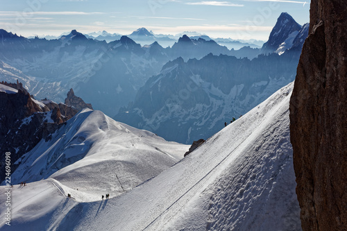 Chamonix, south-east France, Auvergne-Rhône-Alpes. Climbers heading for Mont Blanc. Descending from Aiguille du Midi cable car station towards sunny snow planes and glaciers on border of France