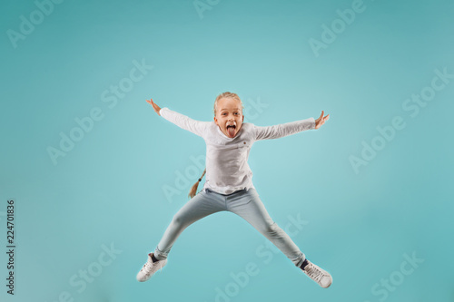 Adorable small child at blue studio. The girl is jumping and smiling. Young emotional surprised teen girl. Human emotions, facial expression concept.
