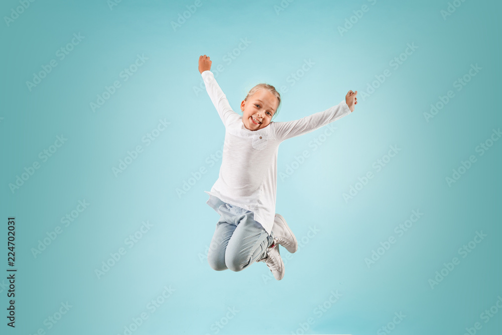 Adorable small child at blue studio. The girl is jumping and smiling. Young emotional surprised teen girl. Human emotions, facial expression concept. Adorable small child at blue studio. The girl is jumping and smiling. Young emotional surprised teen girl. Human emotions, facial expression concept.