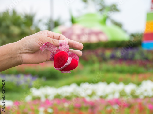 Hand holding red heart on blurred flower background,