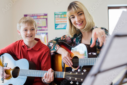 Quadro su tela Teacher Helping Male Student To Play Guitar In Music Lesson