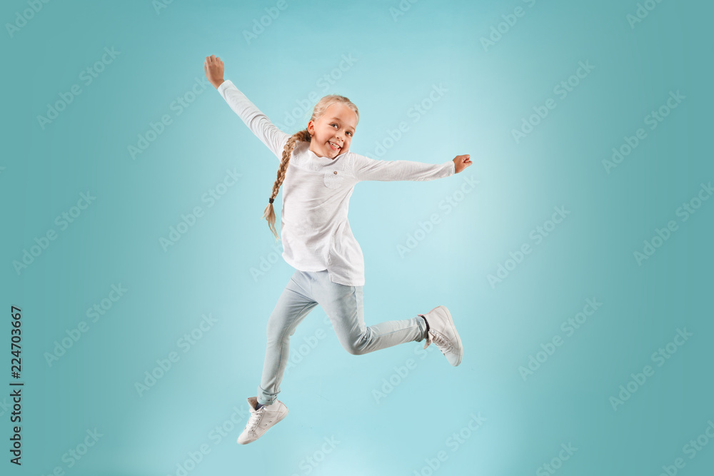 Adorable small child at blue studio. The girl is jumping and smiling. Young emotional surprised teen girl. Human emotions, facial expression concept.