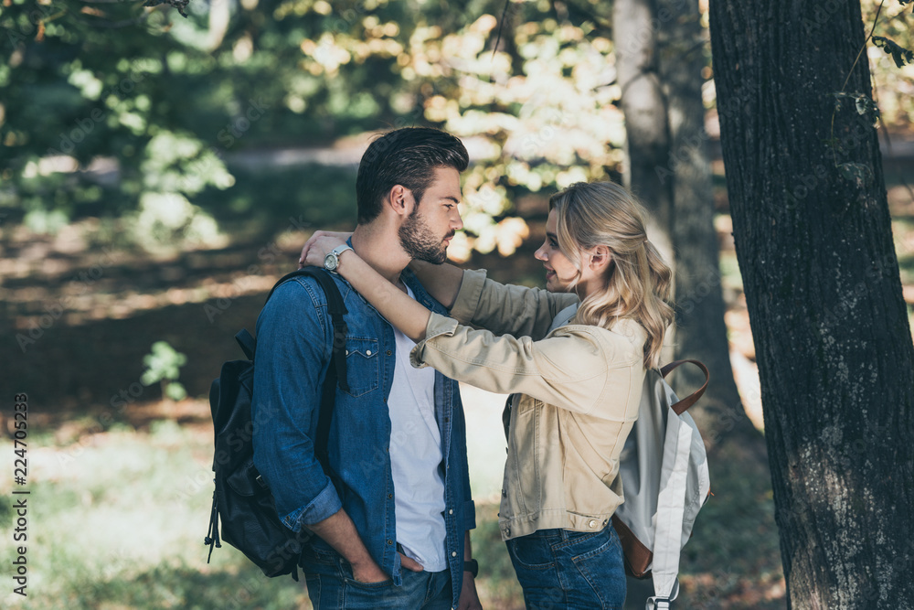 Fototapeta premium young couple with backpacks looking at each other in park