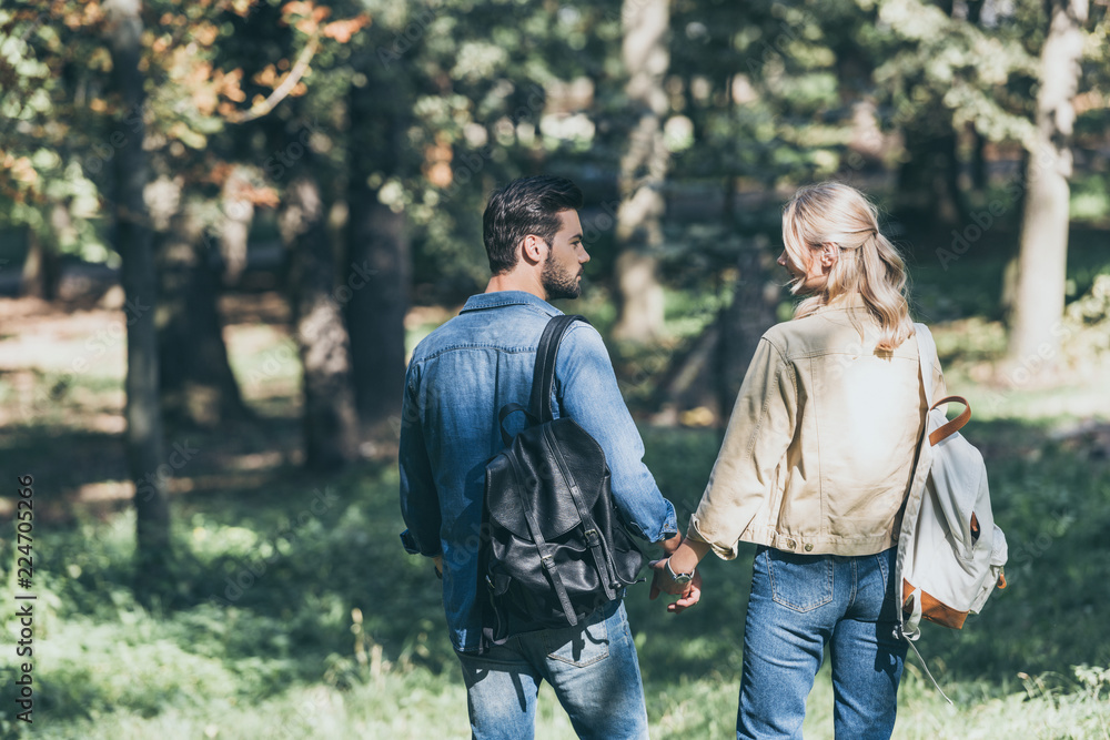 back view of young couple with backpacks walking in autumn park back view of young couple with backpacks walking in autumn park