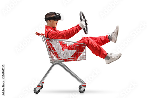 Teenage boy in a racing suit with VR googled holding a steering wheel inside a shopping cart © Ljupco Smokovski