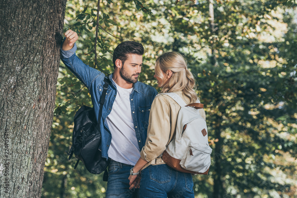 young couple with backpacks looking at each other in park young couple with backpacks looking at each other in park