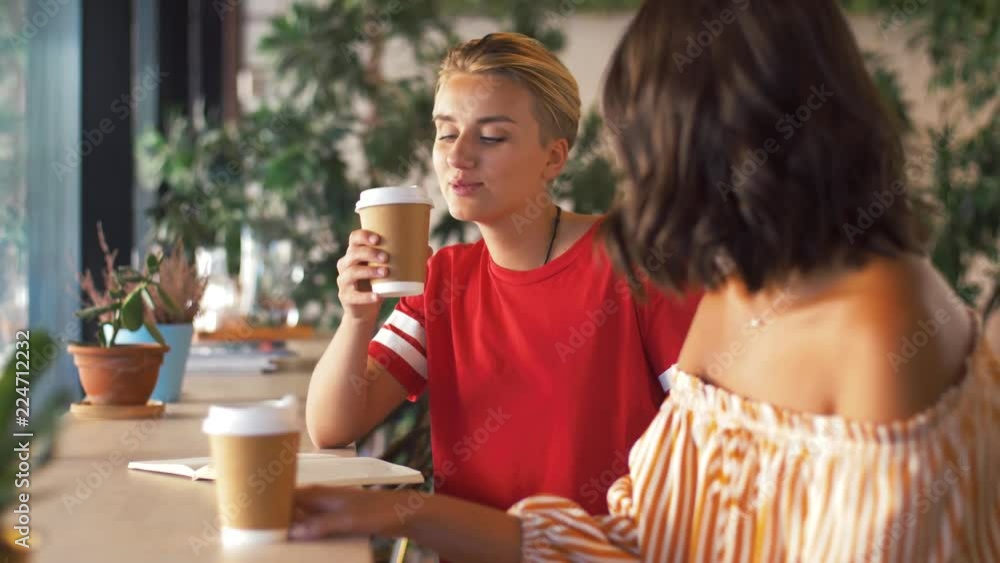 people and friendship concept - young woman with friend drinking coffee drawing to notebook at cafe people and friendship concept - young woman with friend drinking coffee drawing to notebook at cafe