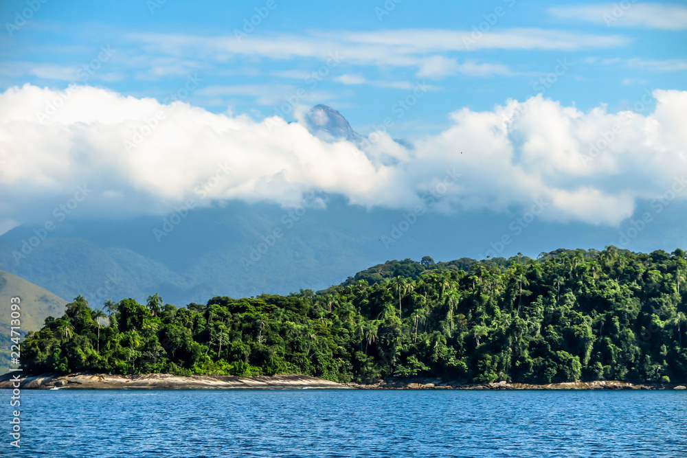Island with tropical forest, blue sea, mountains and clouds in background, Angra dos Reis, Rio de Janeiro, Brazil