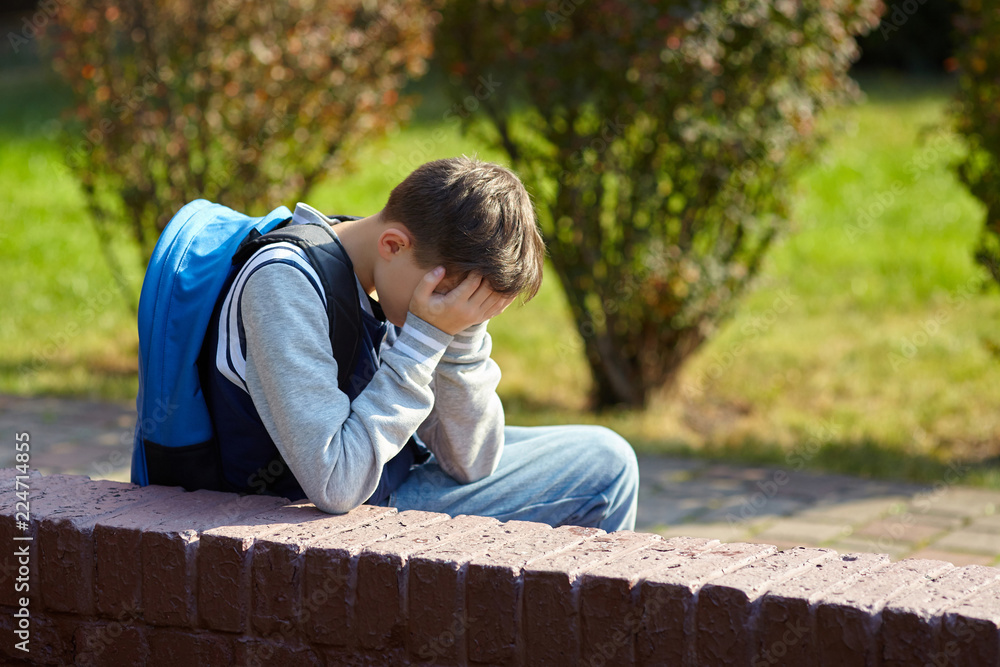 Fototapeta premium Schoolboy crying in the yard of the school