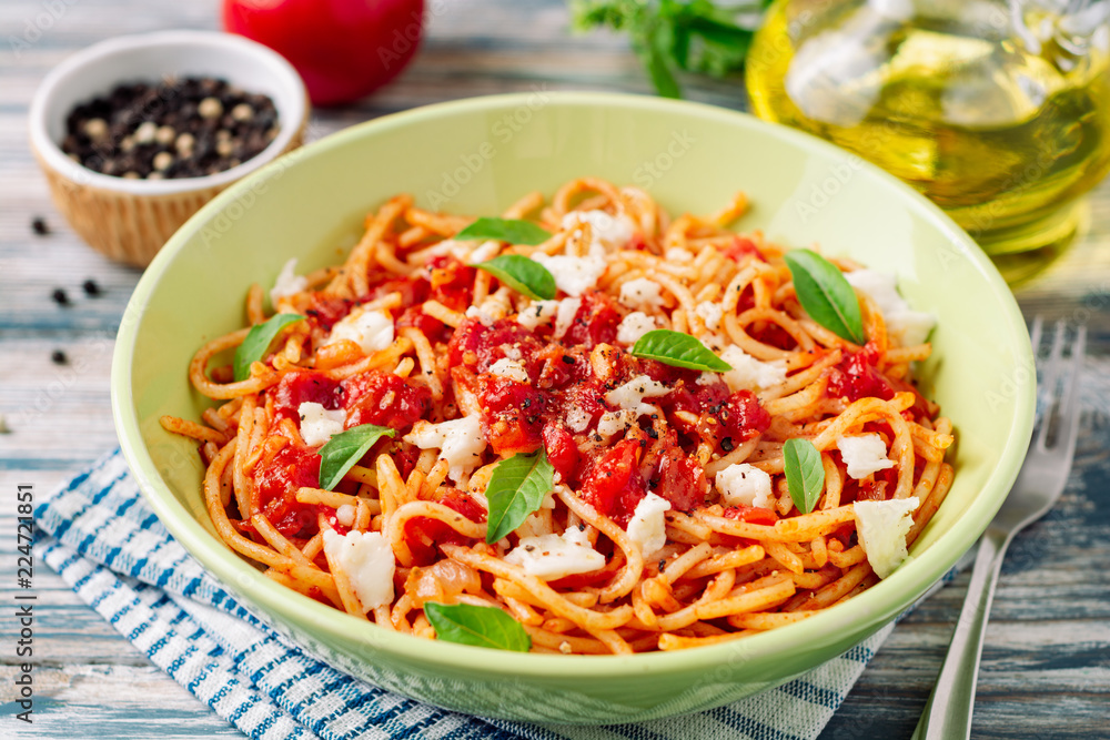 Spaghetti pasta with tomato sauce, mozzarella cheese and fresh basil leaves on white-blue vintage wooden background. Selective focus. Spaghetti pasta with tomato sauce, mozzarella cheese and fresh basil leaves on white-blue vintage wooden background. Selective focus.