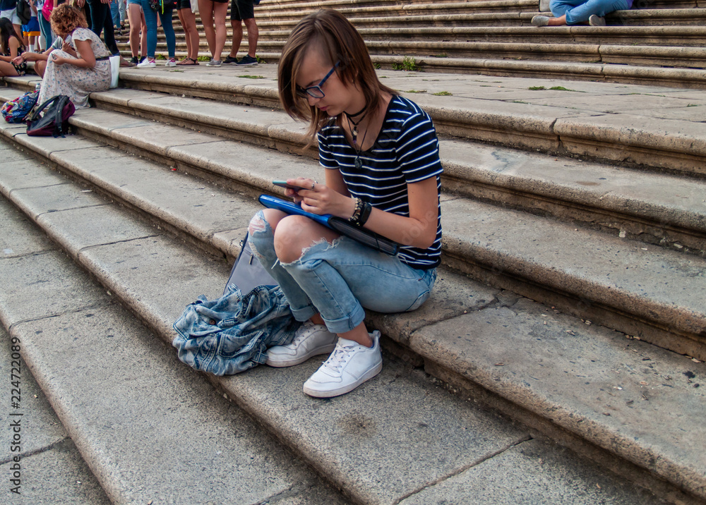 A teenage woman with a smart phone on her hands on the stairs of an historial building A teenage woman with a smart phone on her hands on the stairs of an historial building