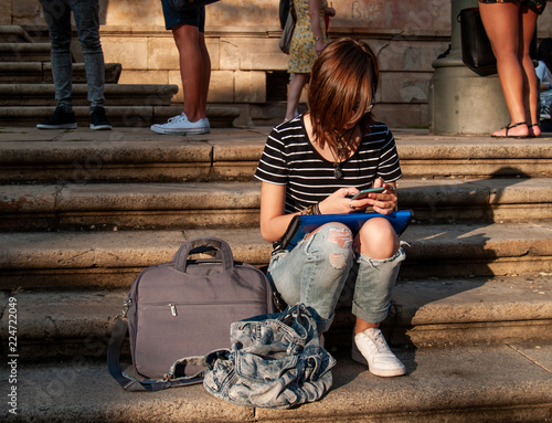 A teenage woman with a smart phone on her hands on the stairs of an historial building