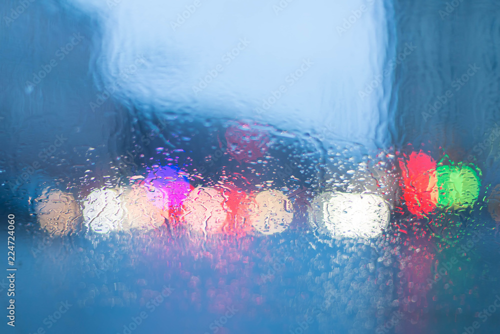Bokeh from illumination of fires of the night city through glass of the car and a rain. Drops of a rain flow down on glass. Indistinct focus