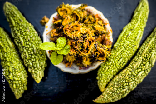 Popular dish for serving in lunch i.e. Bitter gourd with spices and vegetables on wooden surface in a glass plate with raw karela,Close up view. photo