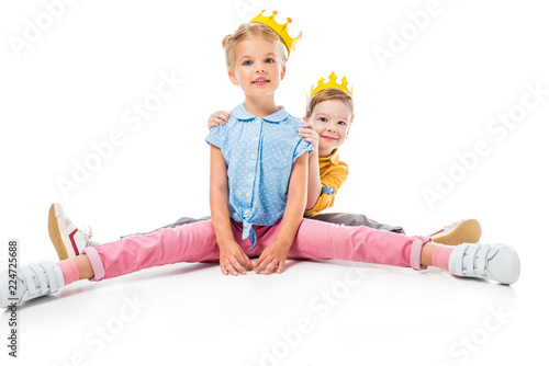 happy siblings in yellow paper crowns sitting together, isolated on white